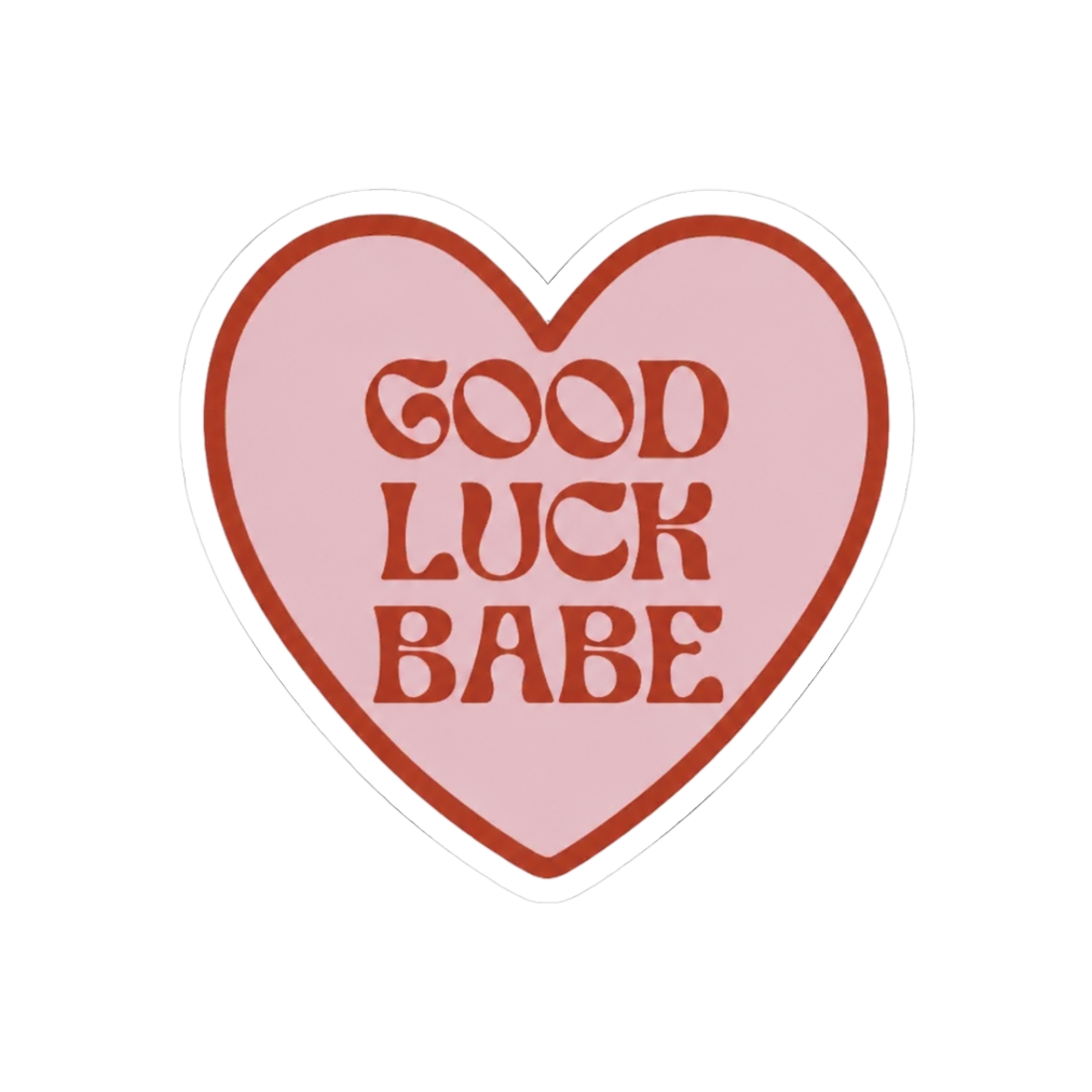A heart-shaped sticker with a pink interior and a dark red border. The sticker features the words "GOOD LUCK BABE" in dark red, retro-style lettering. The sticker is held between two fingers against a...